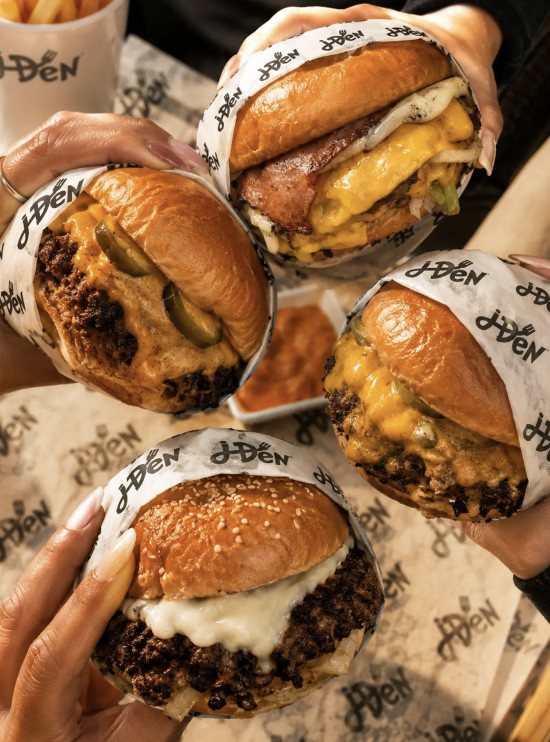 Four J'DEN smash burgers held up in J'DEN wrappers